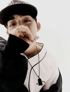 a young man wearing a black hat and holding his finger to his mouth while standing in front of a white background