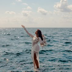 a woman is standing in the water with her arms spread out and she is wearing a white dress