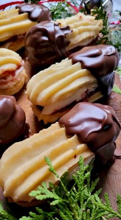 chocolate covered pastries sitting on top of a wooden cutting board next to green leaves