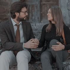 a man and woman sitting on a bench talking to each other in front of an old building