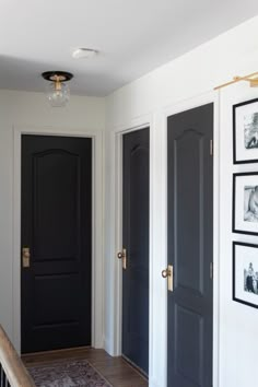 a hallway with black doors and pictures on the wall above it, along with an area rug