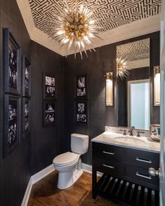 a black and white bathroom with pictures on the wall, chandelier and toilet