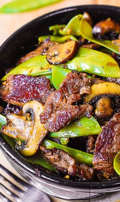 a skillet filled with meat and vegetables on top of a wooden table next to a fork