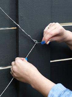 a person is tying something to the side of a building with two hands and blue nails