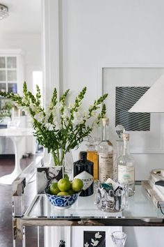 a glass table topped with bottles and glasses next to a vase filled with green apples