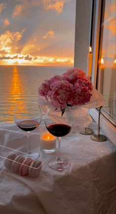 two glasses of wine are sitting on a table with flowers and candles in front of the ocean