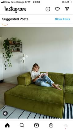 a woman sitting on top of a green couch in front of a white wall and black and white striped rug