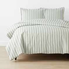 a green and white striped comforter set on a wooden floor in front of a white wall