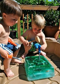 two young boys are playing in an outdoor sand and water play area with green plastic blocks