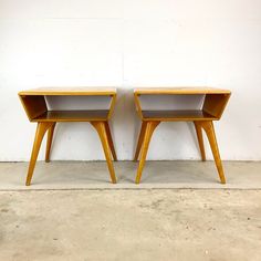 two wooden end tables sitting next to each other on cement floored area with white wall in background