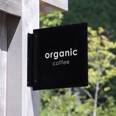 a sign that says organic coffee hanging from the side of a wooden structure with trees in the background