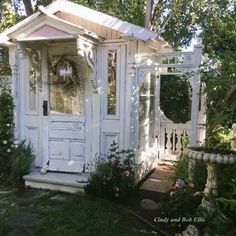 a small white shed sitting in the middle of a garden