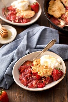 a bowl of strawberry cobbler with ice cream and strawberries next to it on a wooden table