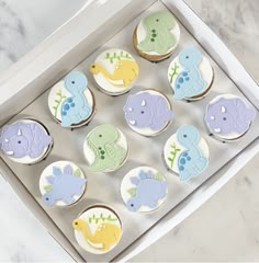 twelve decorated cupcakes in a white box on a marble countertop with blue, yellow and green frosting