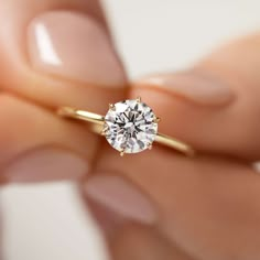 a woman's hand holding an engagement ring with a diamond in the middle, on top of her finger