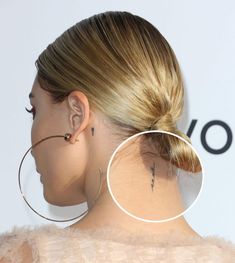 the back of a woman's head with a small tattoo on her left ear