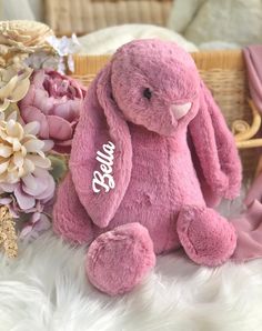 a pink stuffed rabbit sitting on top of a white fur covered floor next to flowers