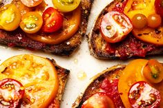 four pieces of toast with tomatoes and cheese on them, sitting on a white surface