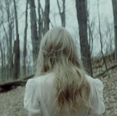 a woman with long blonde hair walking through the woods