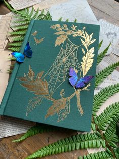 a green book sitting on top of a wooden table covered in papers and butterflies next to it