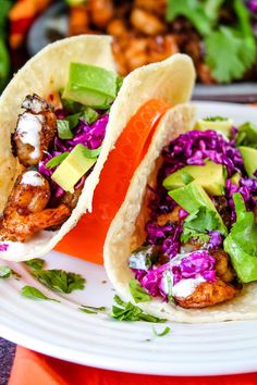 two tacos with shrimp, cabbage and avocado are on a white plate