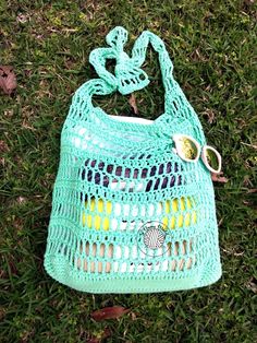 a crocheted bag laying on the grass with a pair of scissors in it