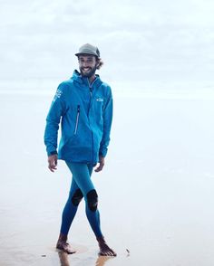 a man standing on top of a beach next to the ocean wearing a wet suit