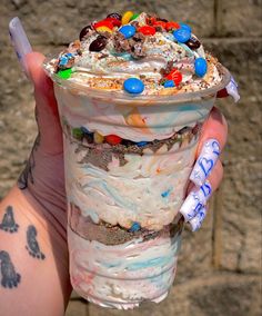 a person holding up an ice cream sundae with candy and candies on it