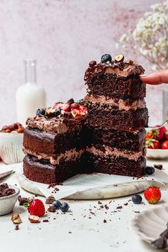 a hand is reaching for a piece of chocolate cake on a plate with strawberries and blueberries