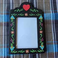 a small black frame with a red heart on the top is sitting on a plaid tablecloth