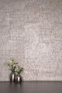 three metal vases with flowers in front of a textured wallpapered background