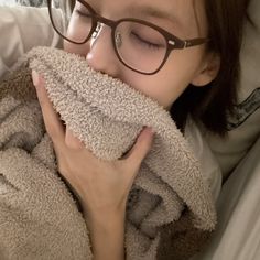 a woman in glasses covers her face with a towel while laying in bed on top of a blanket