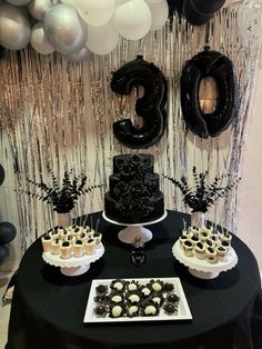 a black table topped with cake and cupcakes next to balloon garlanded wall