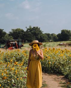 a woman in a yellow dress and hat walking through a sunflower field