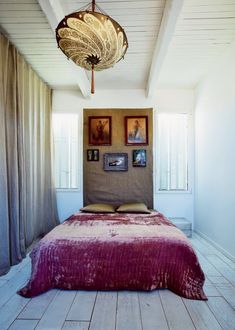 a bed with a red blanket sitting under a light fixture in a bedroom next to two pictures on the wall