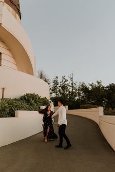 a man and woman walking down a road near a large building with a clock on it