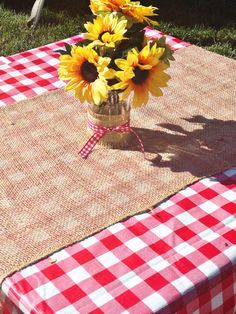 sunflowers in a vase on a picnic table with red and white checkered cloth