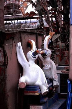 two white rabbits sitting next to each other on top of blue stools in front of a building