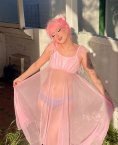 a woman with pink hair and tattoos in a sheer dress posing for the camera outside