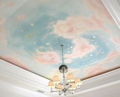 a chandelier hanging from the ceiling in front of a painted sky and clouds mural