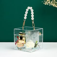 a clear box with pearls and perfume bottles in it on top of a white table