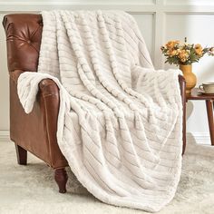 a chair with a blanket on top of it in front of a table and flowers