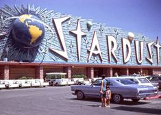 two cars parked in front of a stardust building with a woman standing outside it