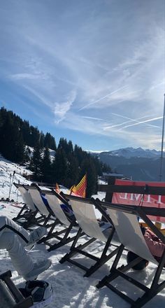 there are many chairs lined up in the snow on top of a hill with mountains in the background