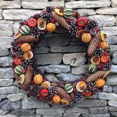 a wreath made out of pine cones, oranges and other autumn decorations on a stone wall