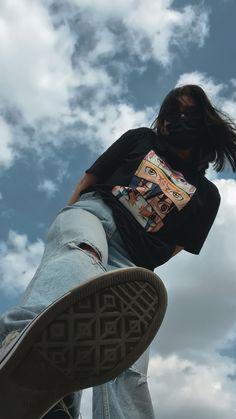 a person in black shirt and blue jeans doing a trick on a skateboard with sky background