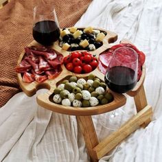 a wooden tray topped with meats, cheese and olives next to a glass of wine