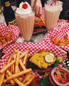 two glasses of milkshakes and some food on a table with red checkered paper