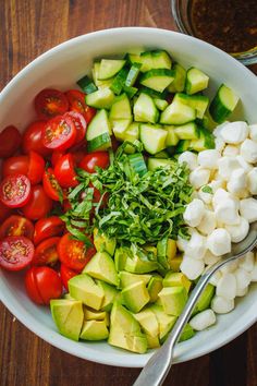 a bowl filled with cucumber, tomatoes, and other veggies next to a spoon