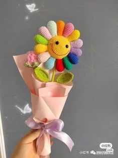 a hand holding a bouquet of crocheted flowers with a smiley face on it